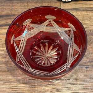 May include: A red glass bowl with a cut crystal design. The bowl has a starburst pattern in the center and a geometric pattern around the rim.