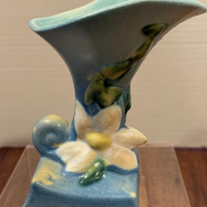 May include: A blue ceramic vase with a flared top and a square base. The vase features a white and yellow flower with green leaves. The vase is approximately 6 inches tall.