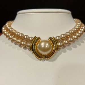May include: A double strand pearl necklace with a gold clasp featuring a large pearl in the center.