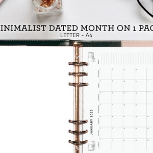May include: A pink leather bound planner with gold rings and a white page with a monthly calendar for January 2023. The calendar is in a minimalist style with only the numbers and days of the week. The planner has colorful tabs for each month.