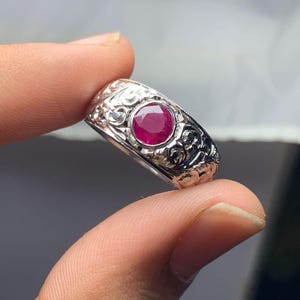 May include: A silver ring with an ornate design and a red ruby gemstone.
