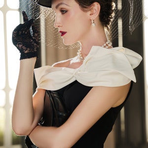 May include: A woman wearing a black dress with a white bow, a black hat with a veil, and black lace gloves. She is holding a black clutch purse. The text "YESTERDAY'S GLAMOUR" is at the bottom of the image.