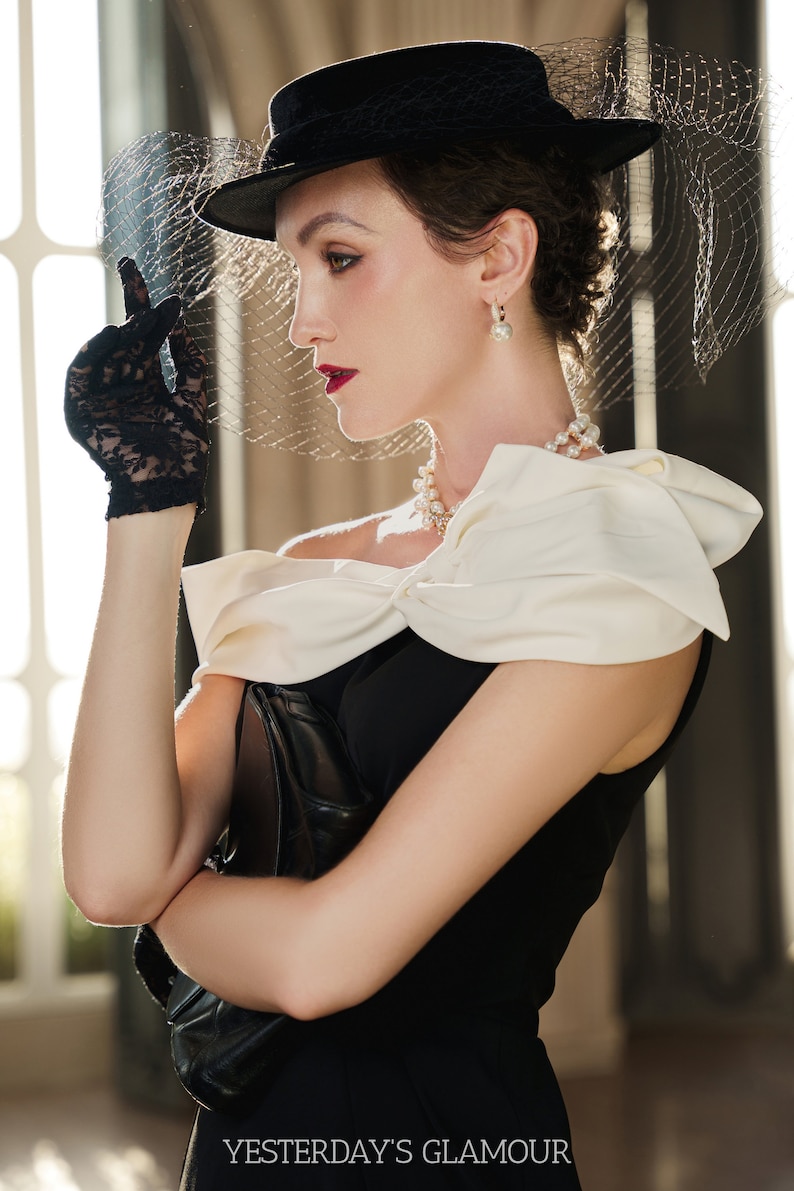 May include: A woman wearing a black dress with a white bow, a black hat with a veil, and black lace gloves. She is holding a black clutch purse. The text "YESTERDAY'S GLAMOUR" is at the bottom of the image.
