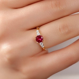 May include: A gold ring featuring a red gemstone surrounded by smaller white gemstones.