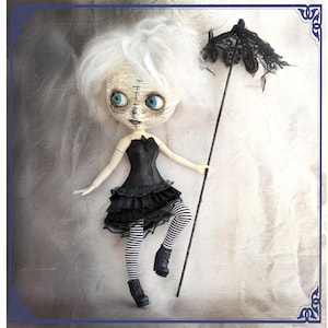 May include: A white-haired doll wearing a black and white dress and black stockings. The doll is holding a black lace umbrella.