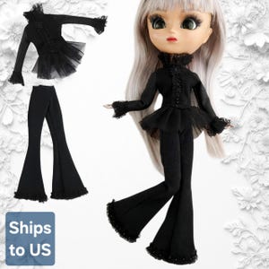 Può includere: Una bambola con lunghi capelli grigio chiaro indossa un top nero a maniche lunghe con colletto alto, dettagli a bottoni e un peplum in tulle arricciato, abbinato a pantaloni neri a zampa. Un completo identico è mostrato a sinistra.