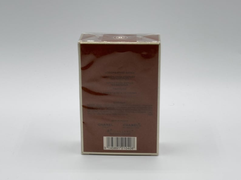May include: A rectangular brown box with a white border, wrapped in clear plastic. The box has text and a barcode on the front. The top of the box has a logo. The box is on a white background.