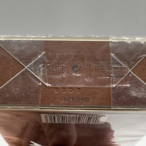 May include: A brown cardboard box wrapped in clear plastic. The box has the numbers "9302" and "121.060" printed on it. The box is sealed with clear tape in a crisscross pattern.
