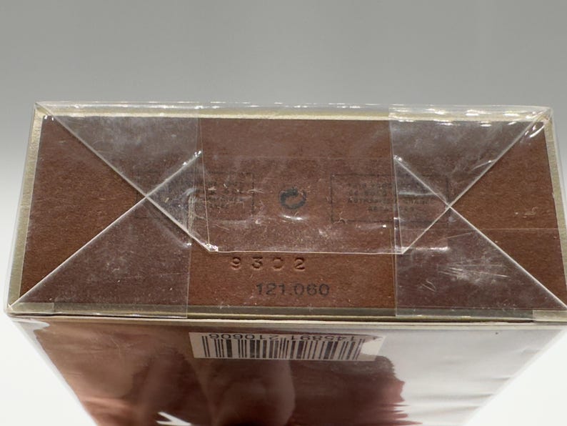 May include: A brown cardboard box wrapped in clear plastic. The box has the numbers "9302" and "121.060" printed on it. The box is sealed with clear tape in a crisscross pattern.