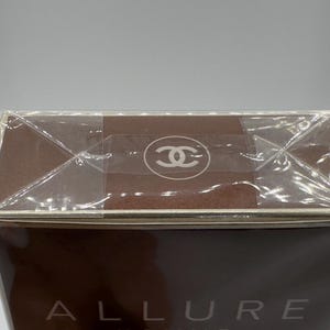 May include: A brown rectangular box with the word "ALLURE" visible. The top of the box is sealed with clear plastic and a logo is visible on the top. The box has a brown color.