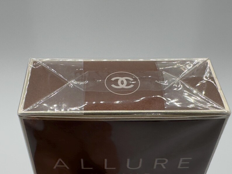 May include: A brown rectangular box with the word "ALLURE" visible. The top of the box is sealed with clear plastic and a logo is visible on the top. The box has a brown color.