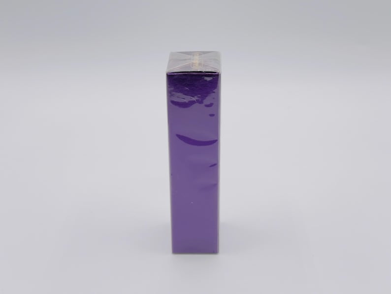 May include: A tall, rectangular, purple box wrapped in clear cellophane. The box is standing upright against a white background. The cellophane is crinkled, and the box is a solid, vibrant purple color.