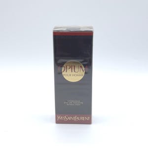 May include: A rectangular box of Yves Saint Laurent Opium Pour Homme Eau de Toilette Natural Spray. The box is primarily black with a gold circular label that reads "Opium Pour Homme". The bottom of the box is red, and the brand name is printed in red.