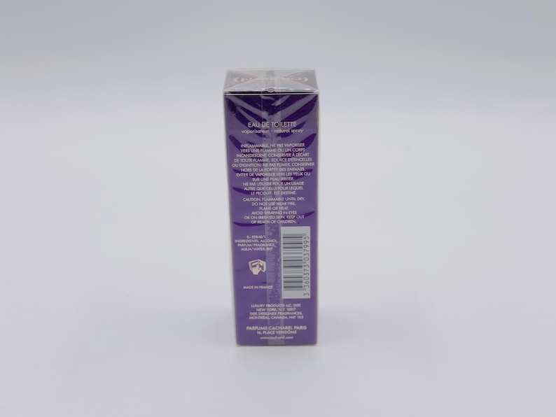 May include: A rectangular, purple perfume box with text in white. The box is sealed in clear plastic. The text includes "EAU DE TOILETTE" and other product information. A barcode is visible on the side.