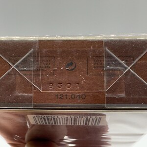 May include: Close-up of a brown cardboard box with a clear plastic wrap. The box has a barcode and the numbers "9301" and "121.040" printed on it. The box is sealed with clear tape.