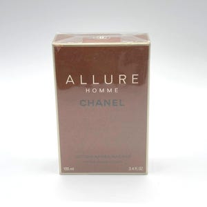 May include: A rectangular box of Chanel Allure Homme after shave lotion. The box is brown with white text that reads "ALLURE HOMME CHANEL". The bottom of the box reads "LOTION APRES RASAGE" and "AFTER SHAVE LOTION". The box contains 3.4 fl oz of product.