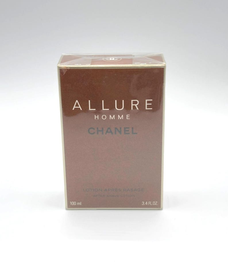 May include: A rectangular box of Chanel Allure Homme after shave lotion. The box is brown with white text that reads "ALLURE HOMME CHANEL". The bottom of the box reads "LOTION APRES RASAGE" and "AFTER SHAVE LOTION". The box contains 3.4 fl oz of product.