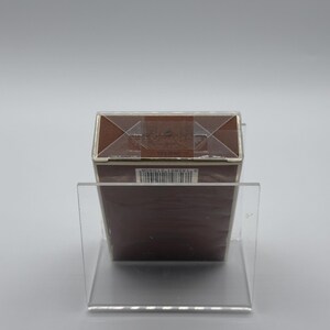 May include: A brown rectangular box with a silver trim, displayed on a clear acrylic stand. The box is sealed with clear tape and has a barcode on the side. The background is a plain, light gray.