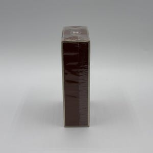 May include: A rectangular, brown box wrapped in clear plastic. The box is a solid, dark brown color and appears to be sealed. The packaging is clean and simple, with no visible labels or text.