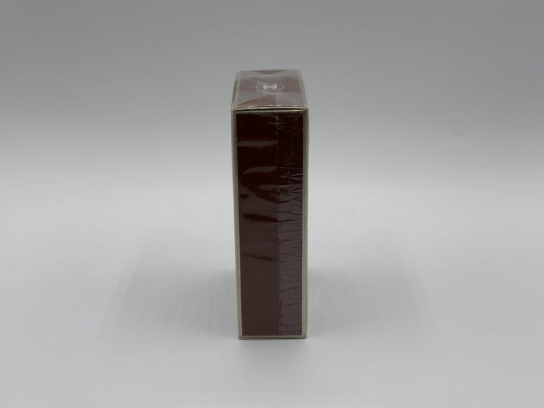 May include: A rectangular, brown box wrapped in clear plastic. The box is a solid, dark brown color and appears to be sealed. The packaging is clean and simple, with no visible labels or text.