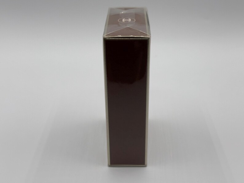 May include: A rectangular, dark brown box with a clear plastic top. The box has a glossy finish and a small, circular logo on the top. The box is standing upright against a white background.