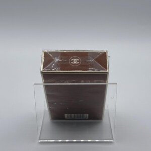 May include: A brown rectangular box with a gold trim and a clear plastic wrap. The top of the box features a white logo. The box is displayed on a clear acrylic stand.