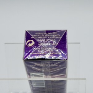 May include: A purple perfume box with white text and a recycling symbol. The text includes the words "DISTRIBUTION EXCLUSIVE" and "PARFUMS CACHAREL PARIS". The box is on a clear shelf.