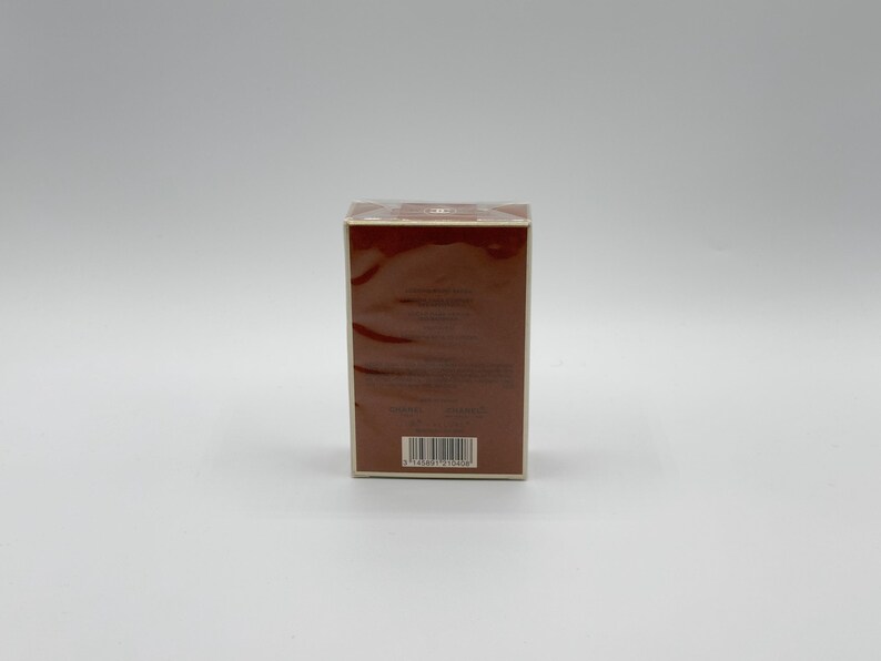 May include: A rectangular brown box with a barcode on the bottom. The box is wrapped in clear plastic and has a light brown border. The background is a plain white surface.
