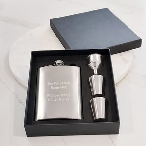 May include: A silver stainless steel hip flask set with two shot glasses and a funnel. The flask is engraved with the text "Jim Barry Oken Happy 60th With love always Gill & Dave xx".