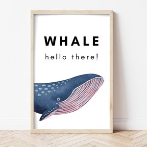 Może przedstawiać: Drukowana grafika ścienna przedstawiająca akwarelowe przedstawienie niebieskiego wieloryba z różowym spodem. Tekst "WHALE hello there!" jest wydrukowany czarnym kolorem u góry grafiki.