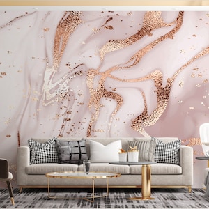 May include: A living room interior design featuring a light pink and gold marble wallpaper, a beige sofa with cushions, a gold coffee table, a gold floor lamp, and a gold side table with a white lamp.
