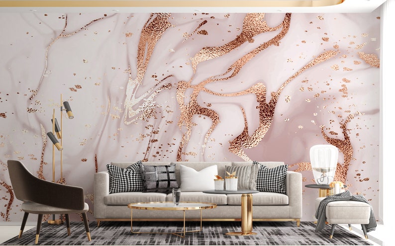 May include: A living room interior design featuring a light pink and gold marble wallpaper, a beige sofa with cushions, a gold coffee table, a gold floor lamp, and a gold side table with a white lamp.