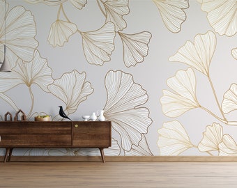 Könnte beinhalten: Ein Wohnzimmer-Interieur mit einer hellgrauen Wand, die mit einer gold-weißen Ginkgoblatt-Mustertapete verziert ist. Ein grauer Sessel steht vor einem Holz-Konsolentisch mit Dekoartikeln.