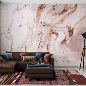 May include: A brown sectional sofa with blue and patterned throw pillows sits in front of a wall with a pink and gold marble wallpaper design. A black tripod floor lamp is in the corner of the room.