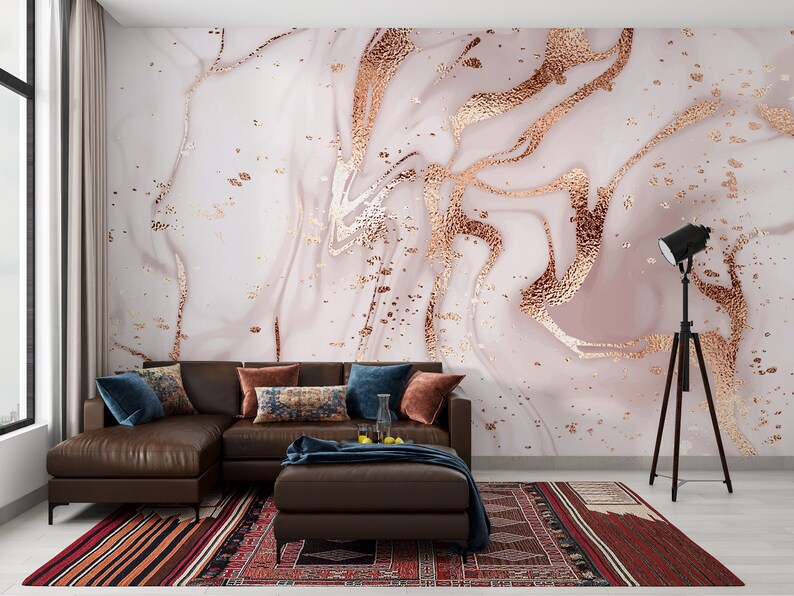 May include: A brown sectional sofa with blue and patterned throw pillows sits in front of a wall with a pink and gold marble wallpaper design. A black tripod floor lamp is in the corner of the room.