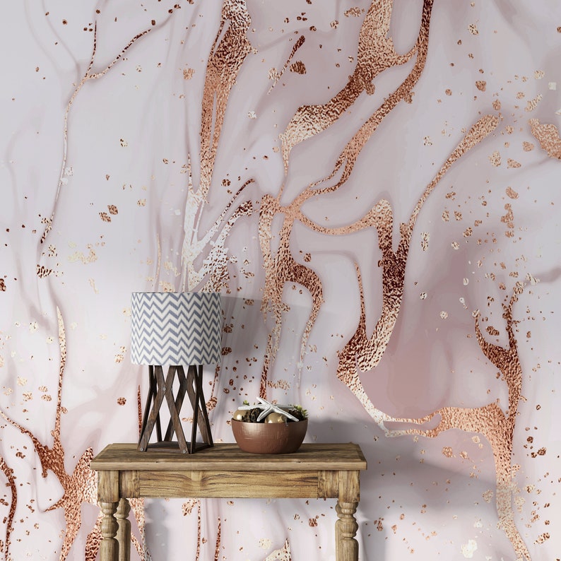 May include: A wooden table with a lamp and a bowl of decorative items. The table is in front of a wall with a pink and gold marble pattern.