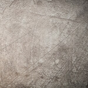 May include: A close-up of a textured, gray surface with a subtle, faded pattern. The surface has a worn, distressed look with visible scratches and marks.