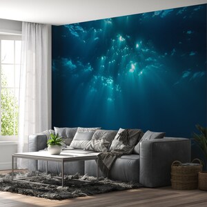 May include: A living room interior design with a gray couch and a coffee table. The wall behind the couch features a large mural of an underwater scene with sunlight shining through the water.