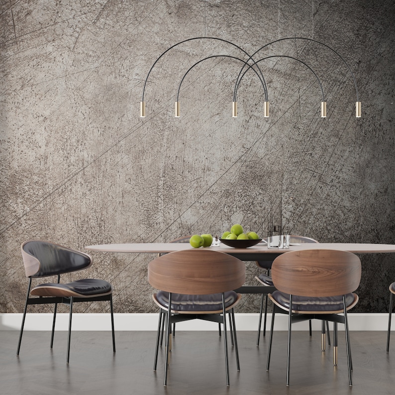 May include: A dining room set with a wooden table and six chairs. The chairs have black metal legs and brown wooden seats. The table has a light wood finish and a black metal base. The wall behind the table is a textured gray with a black metal light fixture hanging from the ceiling.