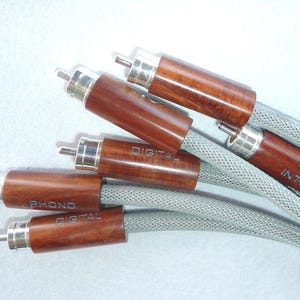 Puede incluir: Primer plano de cinco cables de audio con conectores de madera. Los conectores están etiquetados como "Digital", "Inter", "Phono Digital".