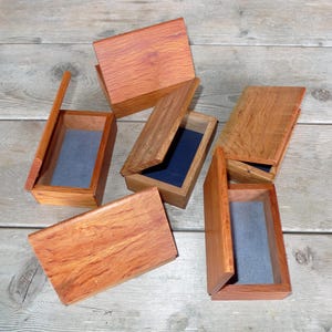 May include: Five wooden boxes with lids, some open, revealing a dark blue interior. The boxes are crafted from light brown wood with a natural grain pattern.