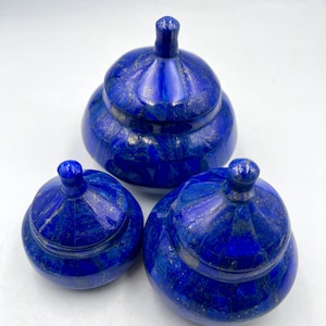 May include: Three blue lapis lazuli lidded boxes of varying sizes. The boxes are made of polished stone and have a speckled appearance.