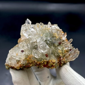 May include: A cluster of clear quartz crystals with a reddish-brown mineral embedded in the matrix. The crystals are sharp and well-defined, with a glassy luster. The matrix is a dark brown color and has a rough texture.