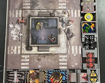May include: A board game with a gray and white game board, red and black dice, and a variety of cards. The game board features a city street with a building in the center. The cards include "Zombie City" and "Full Immunity".