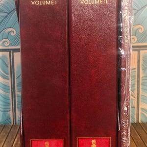 May include: Two red leather-bound volumes of the Lladró Collectors Catalogue, Volume I and Volume II. The books are closed and feature the Lladró Collectors Society logo.