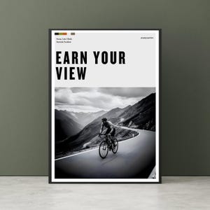 Pode incluir: Pôster emoldurado em preto com o texto "EARN YOUR VIEW" acima de uma imagem em preto e branco de um ciclista em uma estrada de montanha sinuosa. O design do pôster é minimalista, com foco no ciclista e na paisagem.