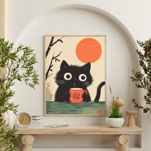 May include: A framed print featuring a black cat holding a red mug with a Japanese-inspired design. The cat is set against a backdrop of a rising orange sun and stylized bamboo branches. The print has a green and beige color palette.