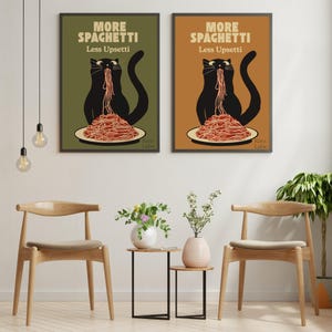 May include: Two framed wall art prints featuring a black cat eating spaghetti from a plate. The text reads MORE SPAGHETTI Less Upsetti. One print has an olive green background, and the other has a warm tan background. Both are displayed side by side.