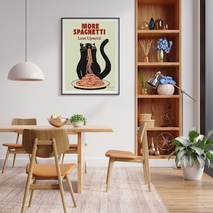 May include: A framed wall art print featuring a black cat eating a plate of red spaghetti with the text More Spaghetti Less Upsetti in red and black lettering on a light green background, displayed in a dining room setting.