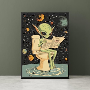 Op de afbeelding: Een ingelijste kunstdruk met een groene alien die op een toilet zit en een krant leest. De achtergrond is een sterrenhemel met planeten. De alien heeft grote ogen en houdt de krant vast. Het toilet is beige.